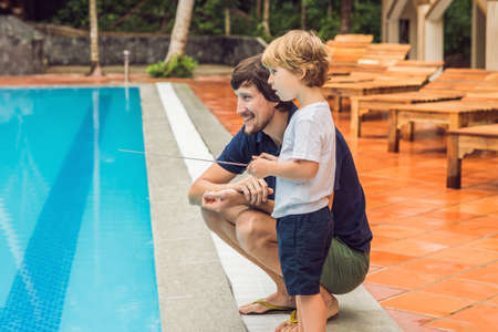 Father and son playing with a remote controlled boat in the pool.の写真素材