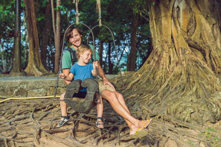 Dad and son swinging on an old swing against the background of the roots of the tree.の写真素材