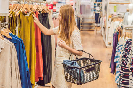sale, fashion, consumerism and people concept - happy young woman with shopping bags choosing clothes in mall or clothing store.の写真素材