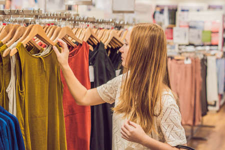 sale, fashion, consumerism and people concept - happy young woman with shopping bags choosing clothes in mall or clothing store.の写真素材