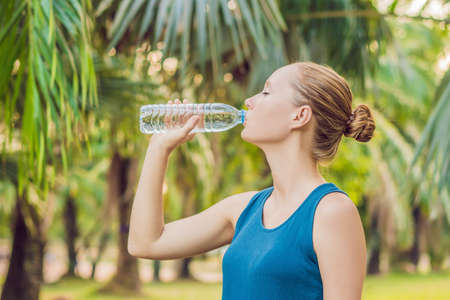 Attractive sporty woman drinking water from a bottle after jogging or running.