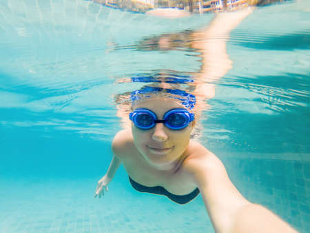 A woman with diving glasses is swimming in the pool under the water.