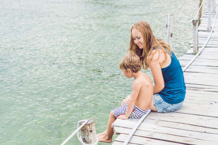 Mom and son are sitting on the old pier and enjoying the sea.の写真素材
