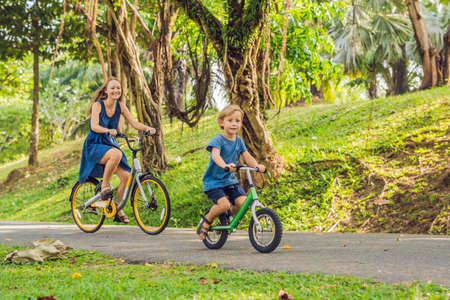 Happy family is riding bikes outdoors and smiling. Mom on a bike and son on a balancebike.の写真素材