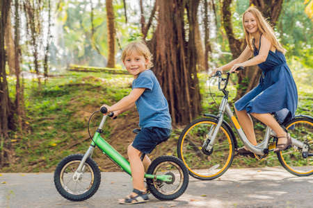 Happy family is riding bikes outdoors and smiling. Mom on a bike and son on a balancebike.の写真素材