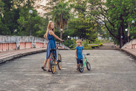 Happy family is riding bikes outdoors and smiling. Mom on a bike and son on a balancebike.