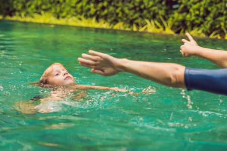 Woman swimming instructor for children is teaching a happy boy to swim in the pool.
