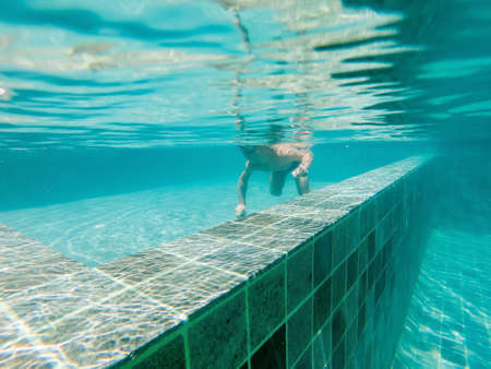 A child boy is swimming underwater in a pool, smiling and holding breath, with swimming glasses.の写真素材