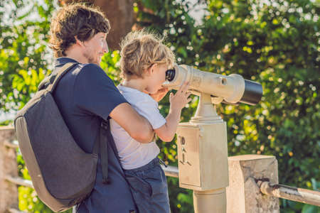 Father and son are looking at Coin-operated binoculars at the sea.