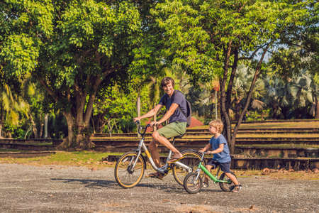 Happy family is riding bikes outdoors and smiling. Father on a bike and son on a balancebike.の写真素材