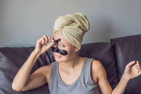 Beautiful young woman relaxing with face mask at home. Happy joyful woman applying black mask on faceの写真素材
