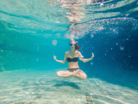 young woman in black bikini in yoga position underwater in diving aquarium, full body shot, front view.の写真素材