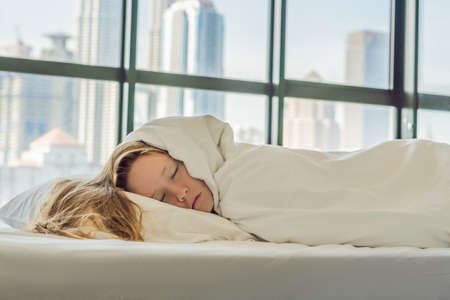 Woman wakes up in the morning in an apartment in the downtown area with a view of the skyscrapers. Life in the noise of the big city concept. Not enough sleep.の写真素材