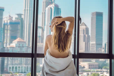 Woman wakes up in the morning in an apartment in the downtown area with a view of the skyscrapers. Life in the noise of the big city concept. Not enough sleep.の写真素材