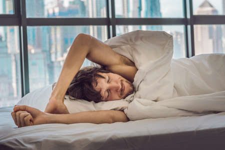 Man wakes up in the morning in an apartment in the downtown area with a view of the skyscrapers. Life in the noise of the big city concept. Not enough sleep.の写真素材