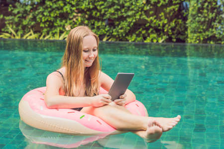 Young female freelancer sitting near the pool with her laptop in the hotel browsing in her...