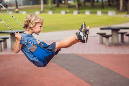 Funny kid boy having fun with chain swing on outdoor playground. child swinging on warm day. Active...