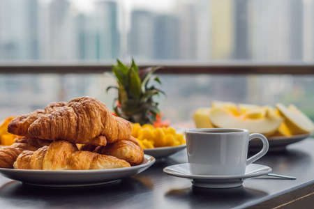 Breakfast table with coffee fruit and bread croisant on a balcony against the backdrop of the big cityの写真素材