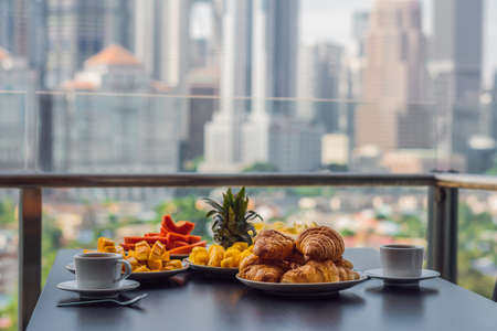 Breakfast table with coffee fruit and bread croisant on a balcony against the backdrop of the big cityの写真素材