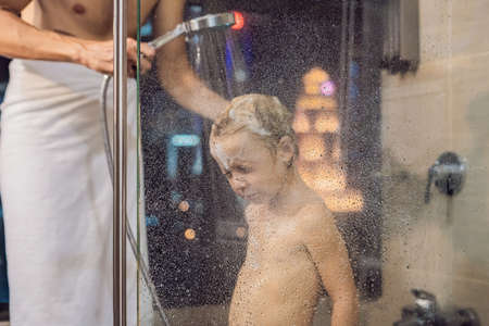 Dad washes his son's hair in the shower in the evening before going to sleep on the background of a window with a panoramic view of the city.の写真素材