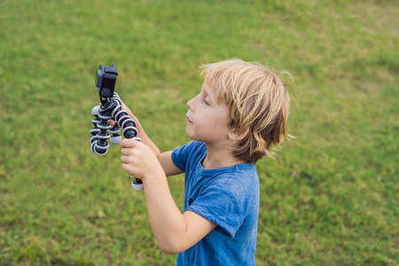 Little boy shoots a video on an action camera against a background of green grass.の写真素材