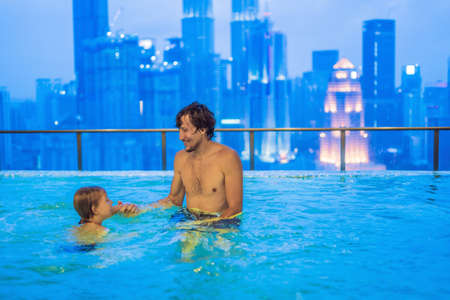 Father and son in outdoor swimming pool with city view in blue sky.の写真素材