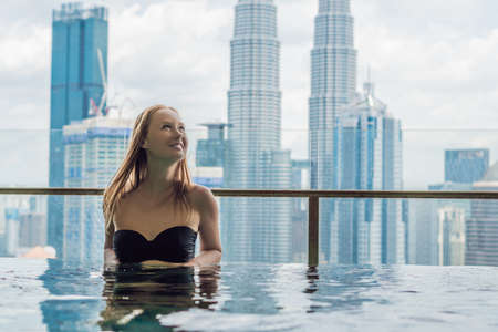 Young woman in outdoor swimming pool with city view in blue sky.