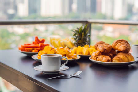 Breakfast table with coffee fruit and bread croisant on a balcony against the backdrop of the big city.の写真素材