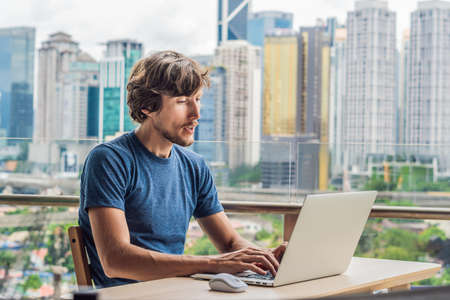 Young man teaches a foreign language or learns a foreign language on the Internet on her balcony against the backdrop of a big city.の写真素材