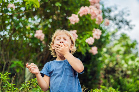 Little boy sneeze in the park against the background of a flowering tree. Allergy to pollen concept.の写真素材