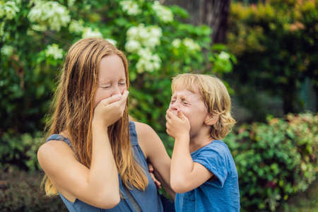 Mom and son sneeze in the park against the background of a flowering tree. Allergy to pollen concept.の写真素材