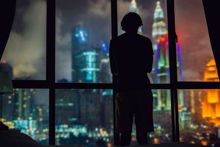 Man looks out the window at the night city.の写真素材