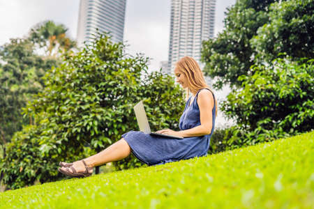 Young smart student female in casual clothes. Woman sitting on grass ground, working on laptop pc computer in city park on green grass sunshine lawn outdoors.の写真素材