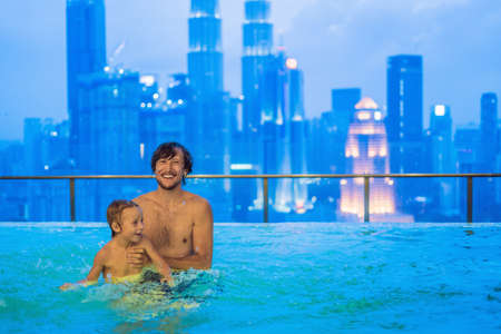 Father and son in outdoor swimming pool with city view in blue sky.の写真素材