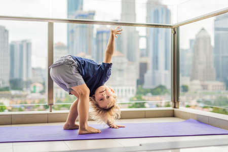 Happy little boy is practicing yoga on his balcony with a panoramic view of the big city.の写真素材