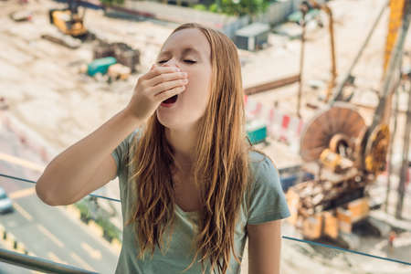 A young woman by the window annoyed by the building works outside. Noise concept.の写真素材