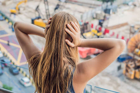 A young woman by the window annoyed by the building works outside. Noise concept.