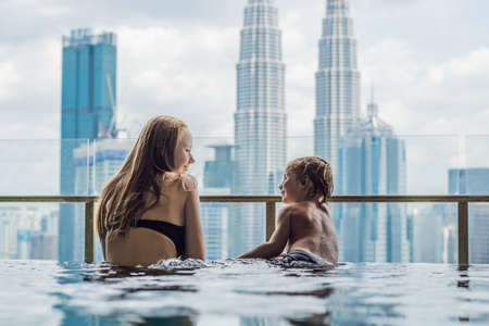 Mother and son in outdoor swimming pool with city view in blue sky.の写真素材