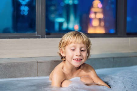 Happy little baby boy sitting in bath tub in the evening before going to sleep on the background of...