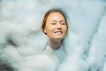 Relaxed young woman lying in bath with foam.