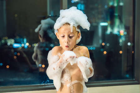 Happy little baby boy sitting in bath tub in the evening before going to sleep on the background of...