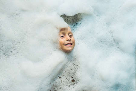 Happy little boy face swimming in the bathroom. Portrait of baby bathing in a bath full of foam.の写真素材