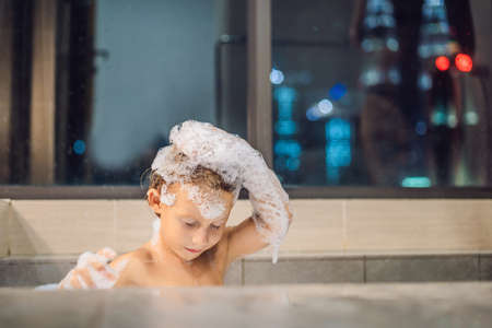 Happy little baby boy sitting in bath tub in the evening before going to sleep on the background of...