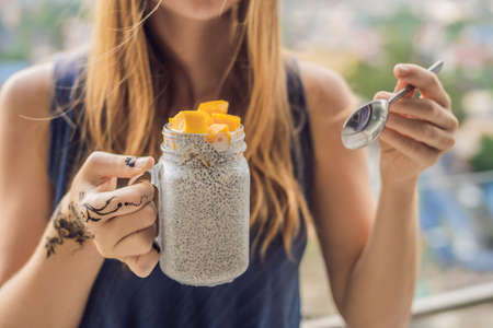 Young woman with mehendi from henna on hand eating chia pudding on her balcony overlooking the big city.の写真素材