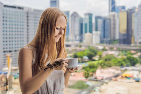 Young woman with a picture on the hand of henna - mehendi drinks coffee in the morning on the balcony overlooking the big city and skyscrapers.の写真素材