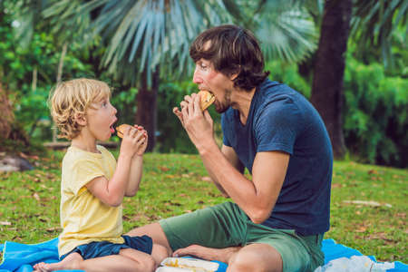 Portrait of a young father and his son enjoying a hamburger in a park and smiling.