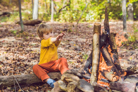 The boy is sitting at the camp fire.