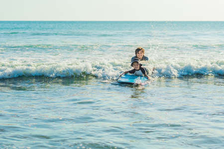 Father teaching his young son how to surf in the sea on vacation or holiday. Travel and sports with children concept.の写真素材