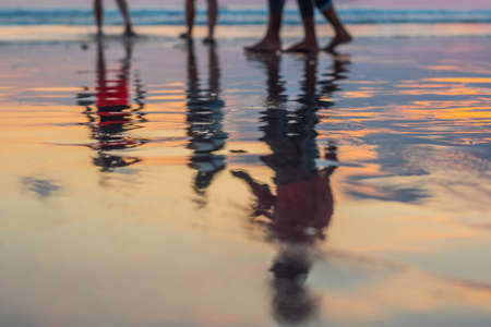 Silhouette of couple walking and talking on beach with drop shadow reflected on calm sea water surface in evening sunset. Holiday vacation, relax and chilling on beach in summer used for background.の写真素材