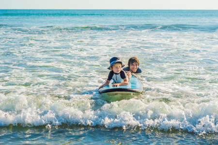 Father teaching his young son how to surf in the sea on vacation or holiday. Travel and sports with children concept.の写真素材